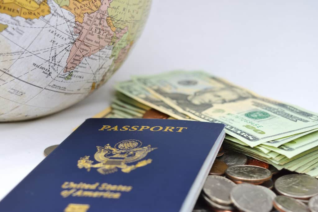 A U.S. passport placed next to a globe and a stack of currency, symbolizing travel and the benefits of FEIE or Form 2555 for managing taxes while living abroad.